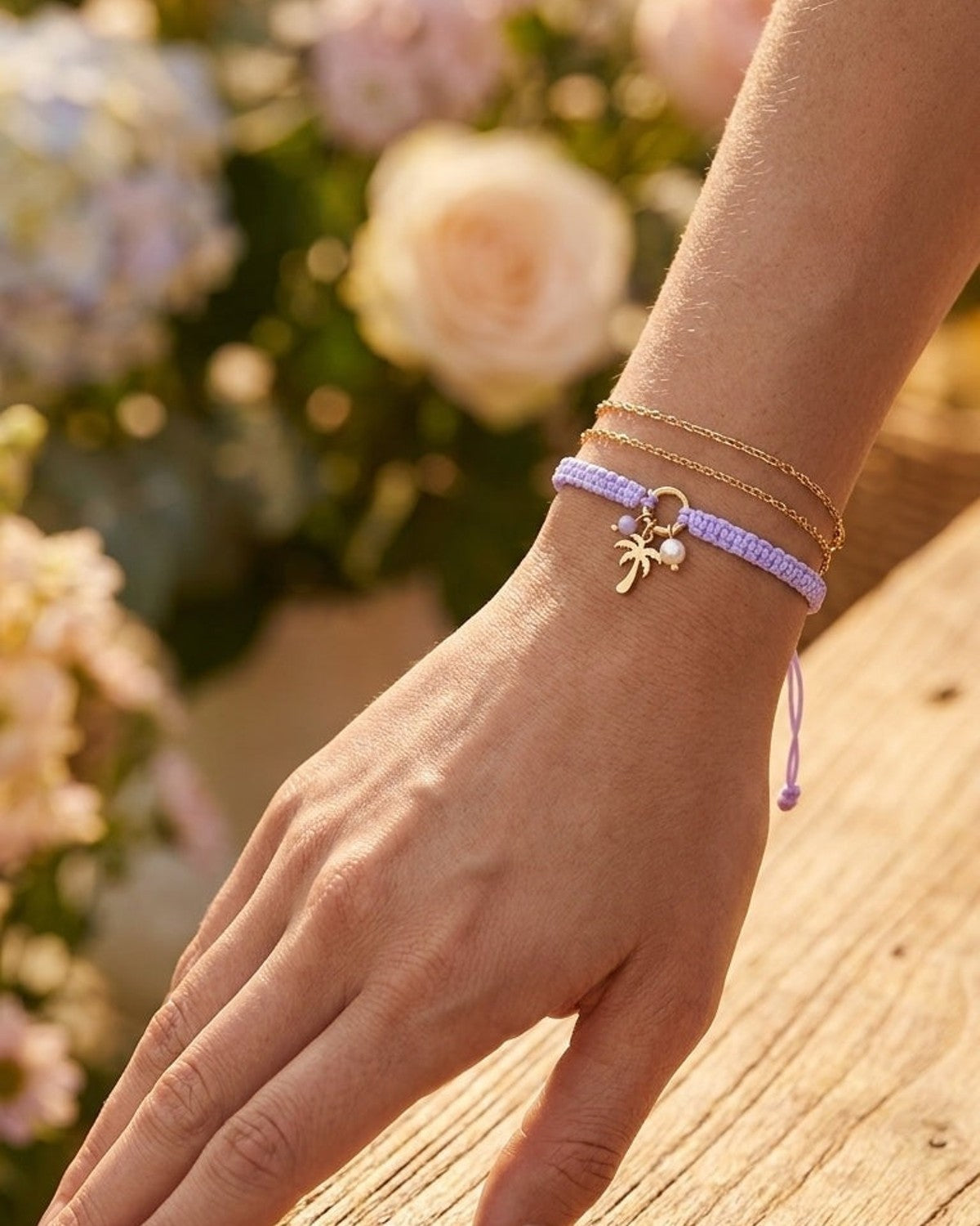 Layered bracelets: a thin gold chain and a braided lavender cord with a palm tree charm.
