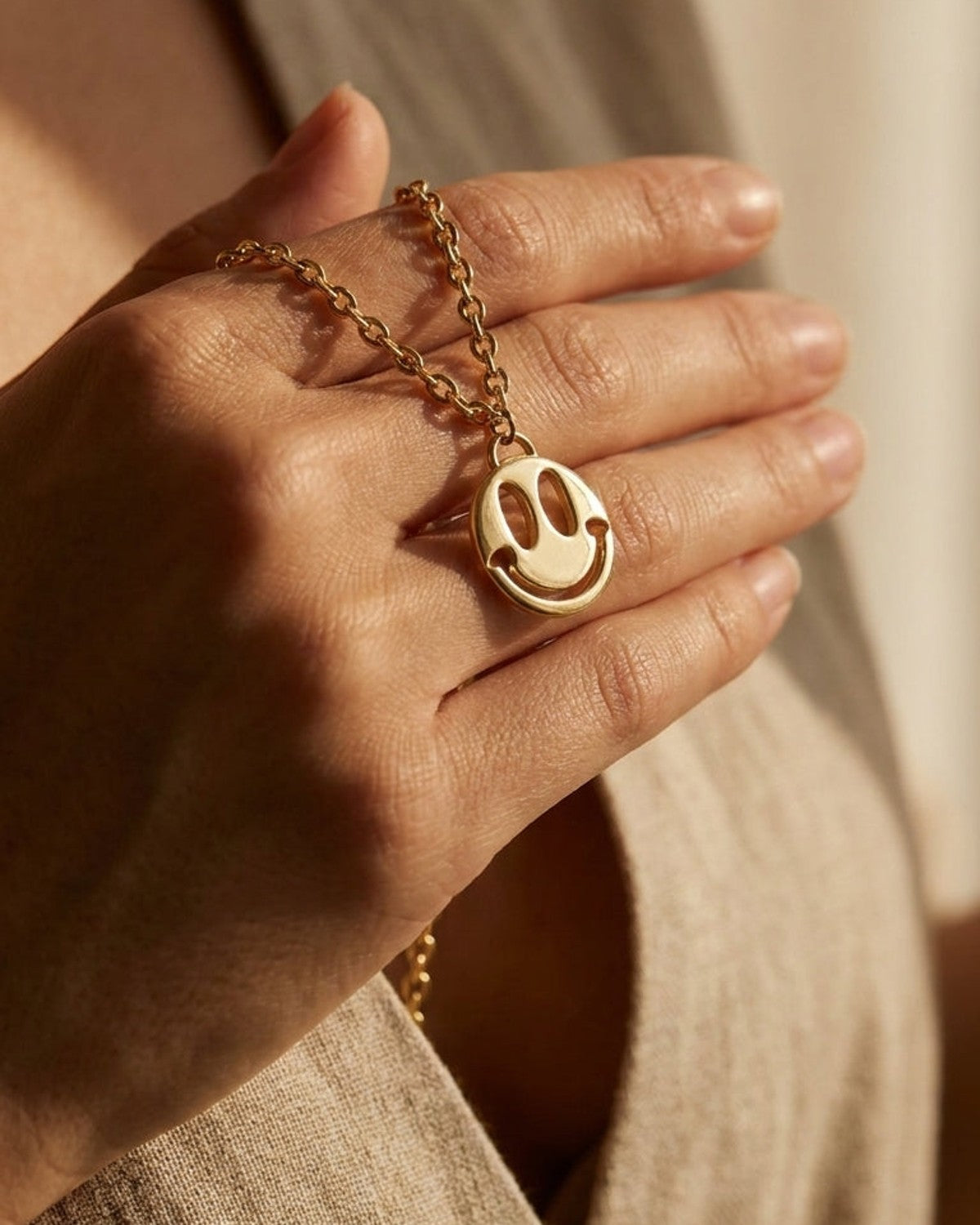 Gold link chain necklace with a smiley face pendant resting on a person's hand.
