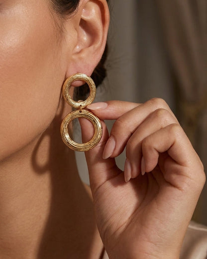 Chic gold circle earrings with a textured finish, worn on a person's ear.