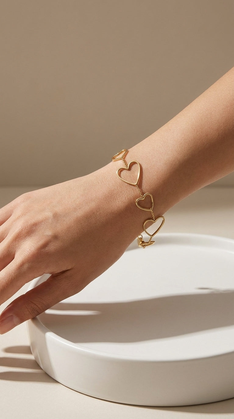 Gold heart charm bracelet worn on a wrist, featuring connected open-work heart shapes in a polished metal finish.