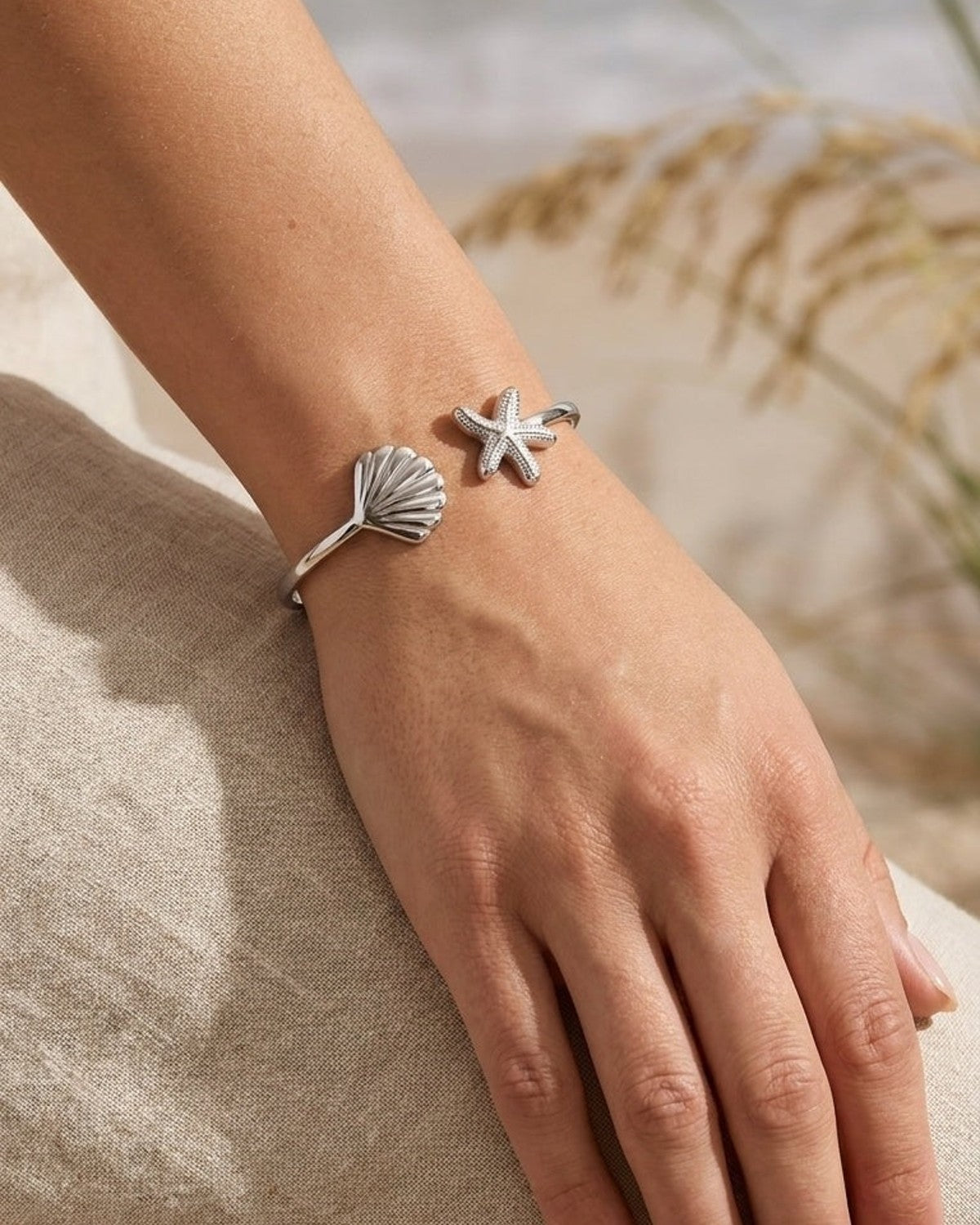 Silver open-cuff bracelet featuring a seashell charm on one end and a textured starfish on the other.