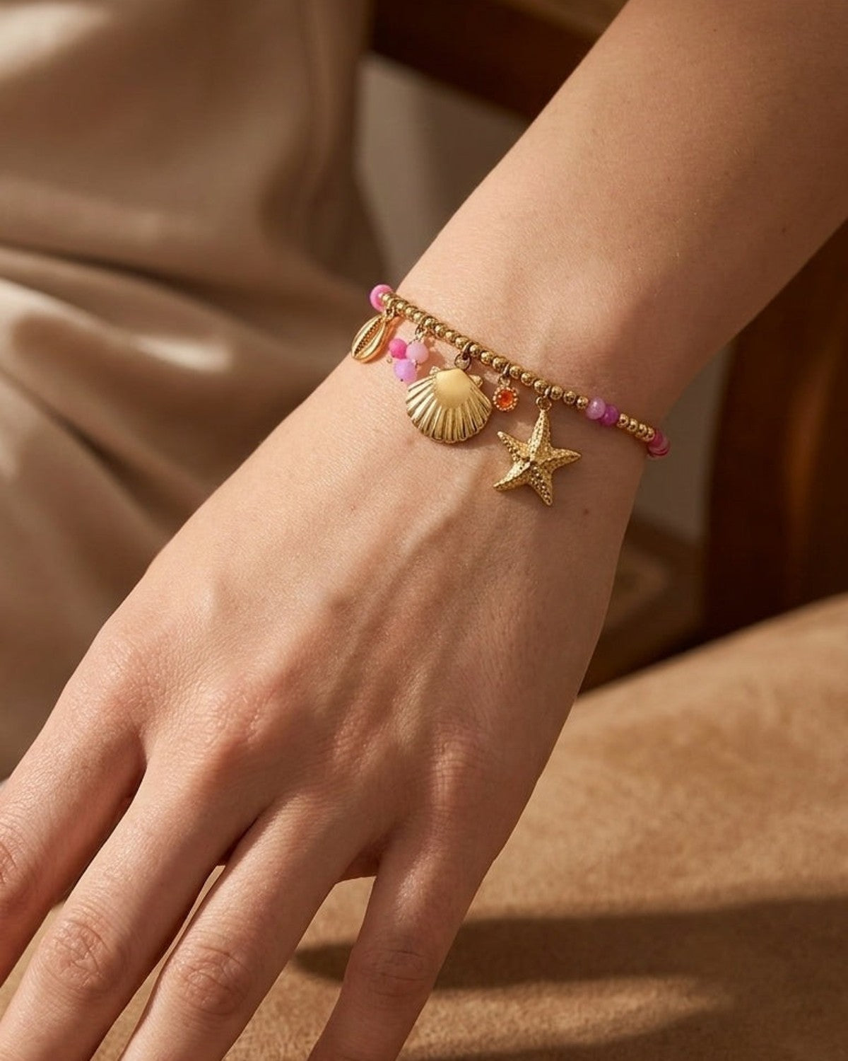 Gold beaded bracelet with dangling seashell and starfish charms, plus pink beads and an orange crystal.