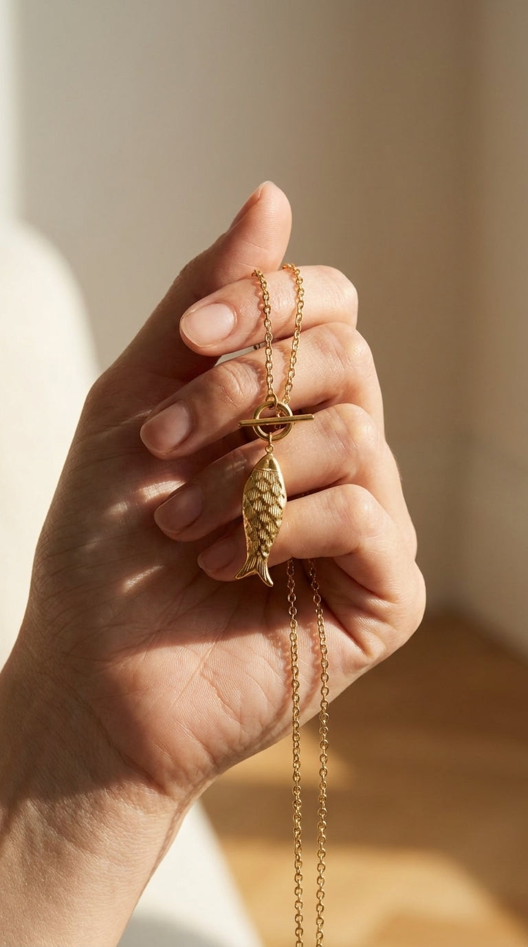 Catching Vibes gold necklace with a textured fish pendant and a delicate toggle clasp held in a hand.