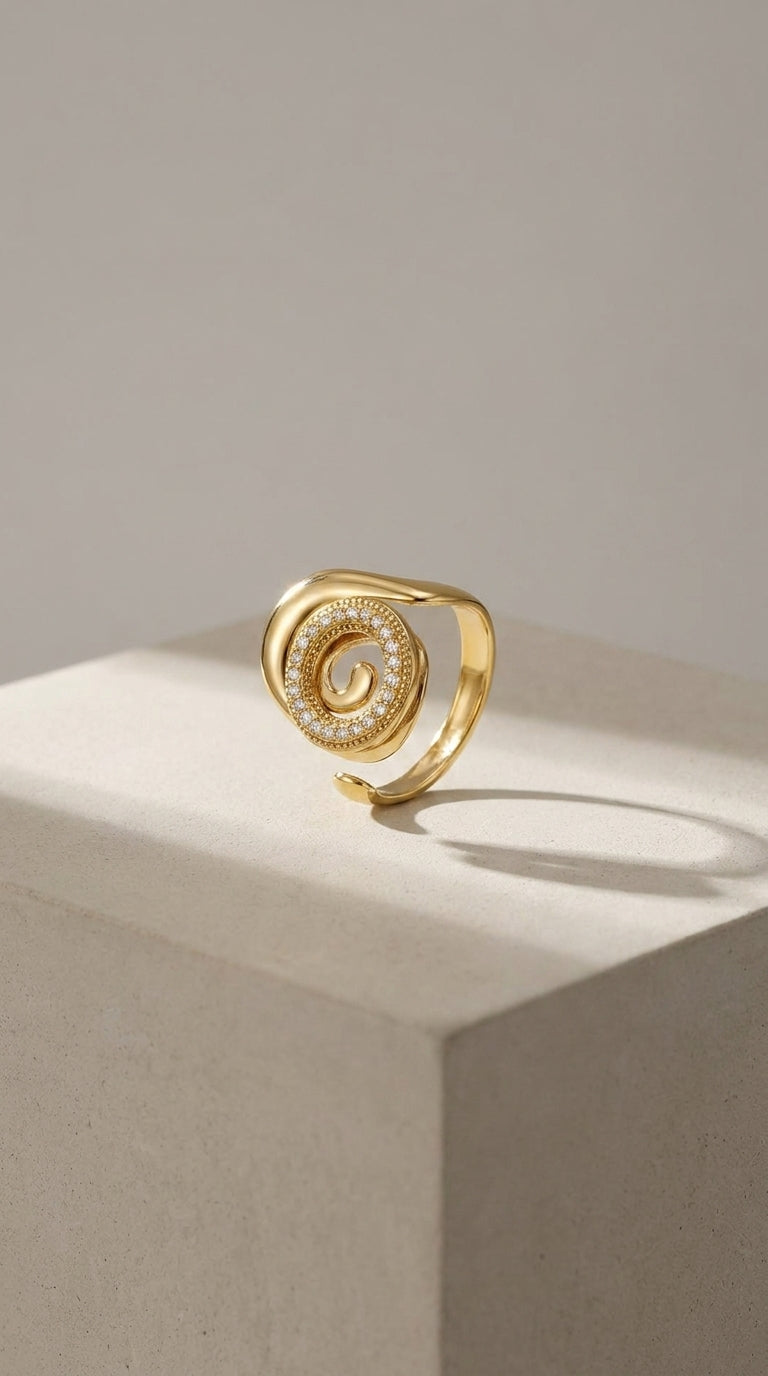 Gold Coastal spiral statement ring with a pavé diamond-encrusted swirl center, displayed on a stone cube.