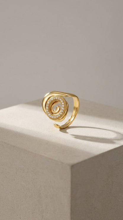 Gold Coastal spiral statement ring with a pavé diamond-encrusted swirl center, displayed on a stone cube.