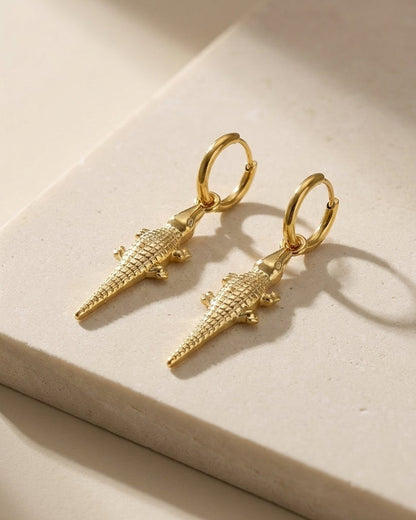 Gold hoop drop earrings featuring textured alligator pendants on a neutral surface.