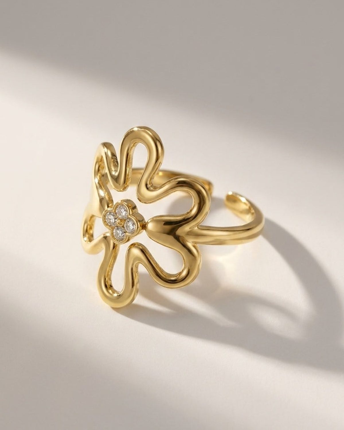 Gold flower-shaped ring featuring a sparkling four-stone cluster center on a neutral surface.