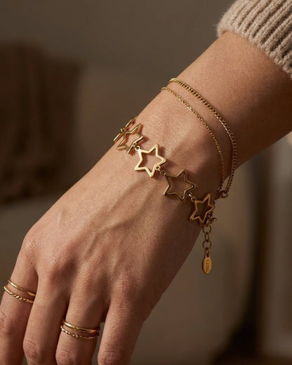 Gold star charm bracelet and double chain worn on a wrist.
