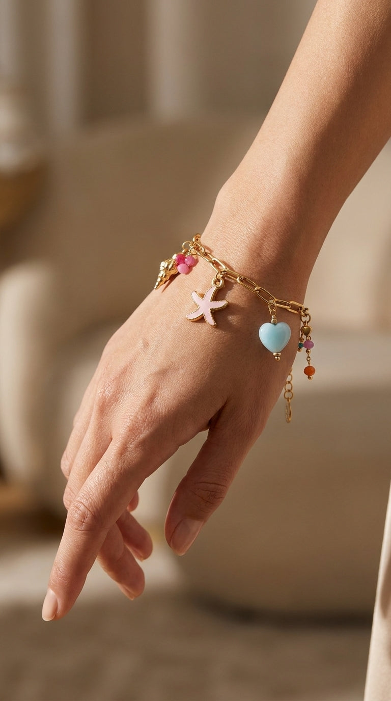 Coastal Charm gold-tone chain bracelet featuring pink starfish, blue heart, and colorful bead charms on a wrist.
