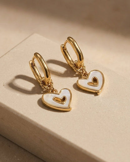 Gold hoop earrings with dangling heart charms inlaid with white mother-of-pearl and a raised gold inner heart.