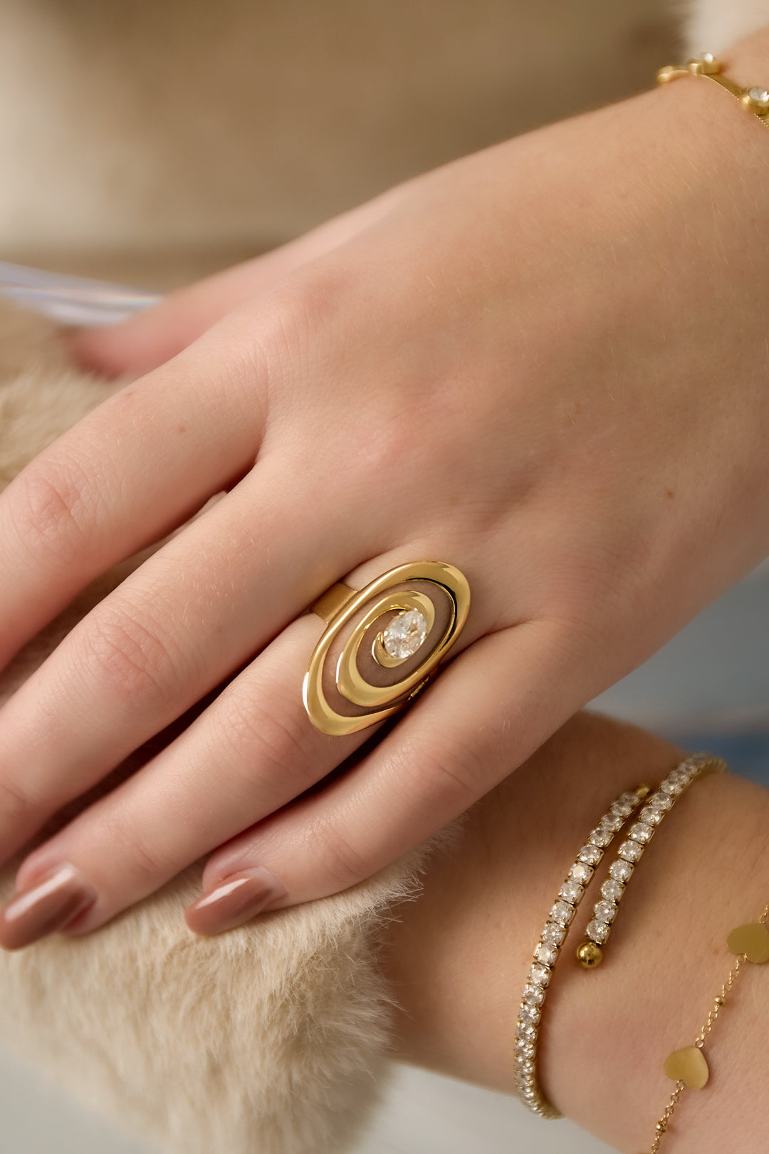Close-up of the gold spiral ring worn on finger alongside delicate gold and gemstone bracelets