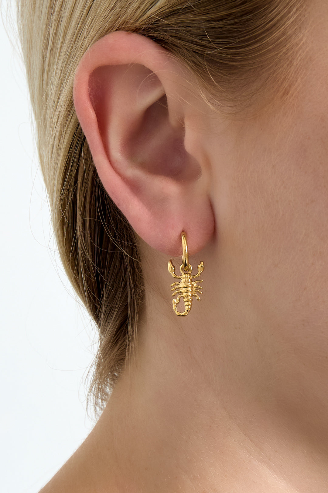 Close-up of a woman wearing a gold hoop earring with a hanging scorpion charm, showcasing fit and style