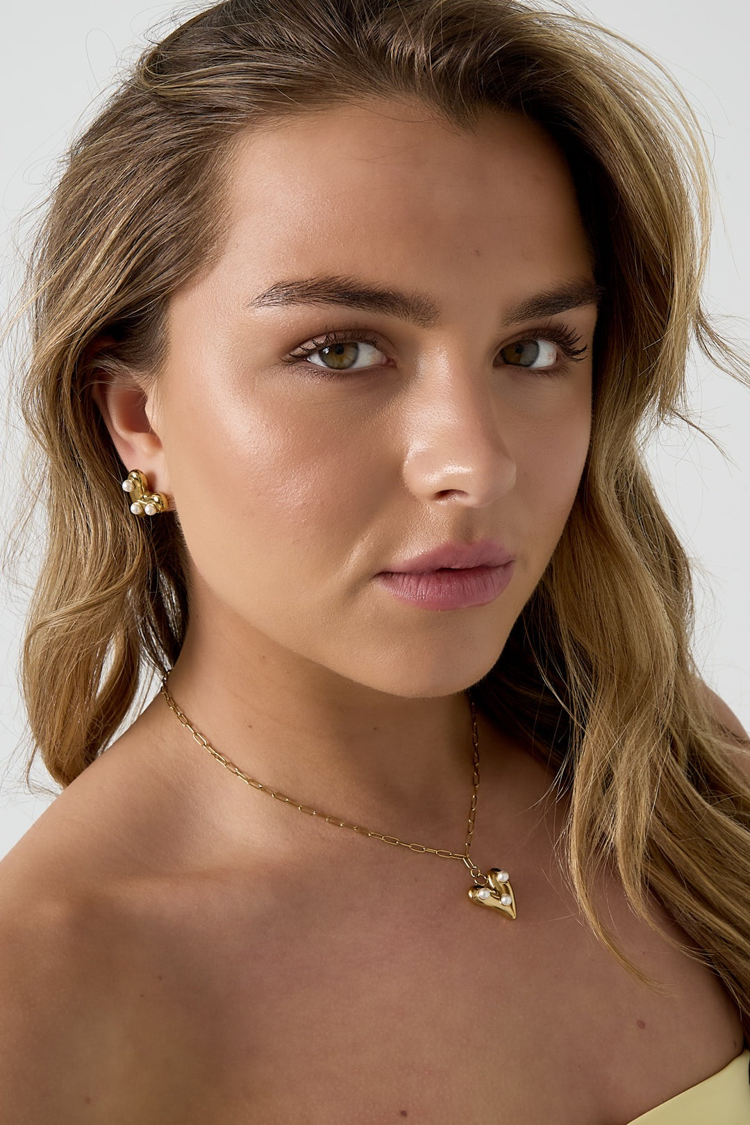 Close-up of a model wearing the gold-tone pearl heart pendant necklace with matching pearl heart earrings