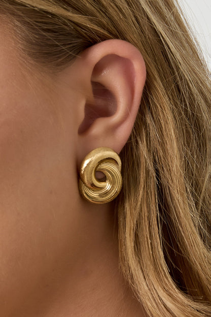 Close-up side view of gold twist stud earring worn on ear highlighting spiral shape and texture