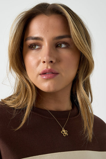 Young woman wearing gold floral pendant necklace with sculptural flower on delicate chain paired with brown top