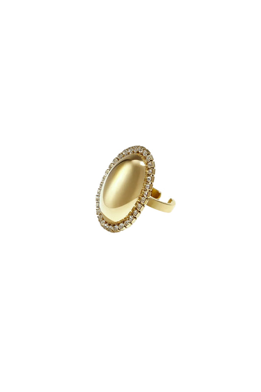 Close-up of a golden oval statement ring with rhinestone border on a white background.