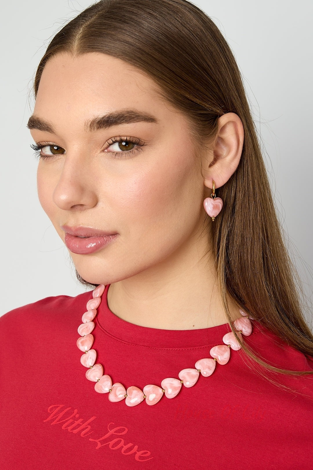 Close-up side profile of model wearing peach resin heart drop earrings with gold hoops
