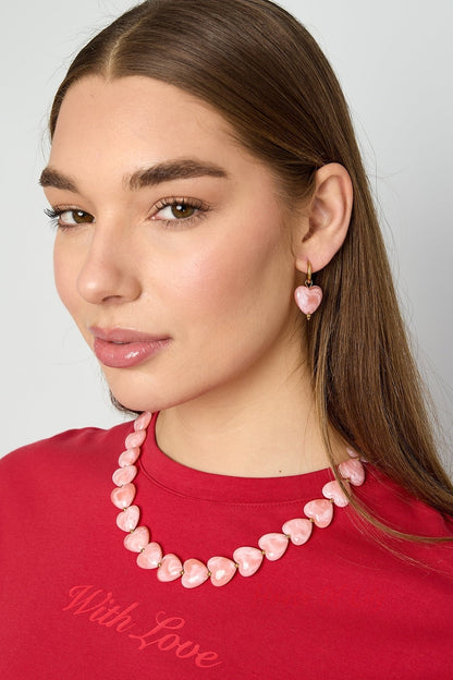 Close-up side profile of model wearing peach resin heart drop earrings with gold hoops