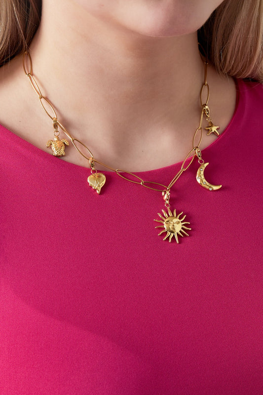 Close-up of playful gold charm link necklace worn by woman in vibrant pink top showing sun, moon, starfish, turtle, and shell charms hanging