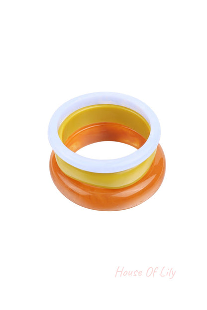 Stack of three resin bangles in light blue, yellow, and marbled orange on white background
