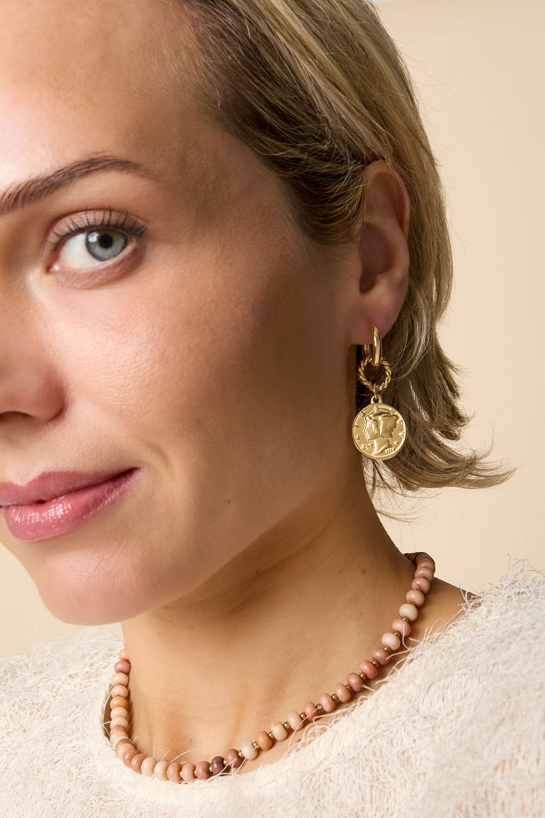 Close-up of woman wearing a gold vintage coin hoop earring paired with a pink bead necklace