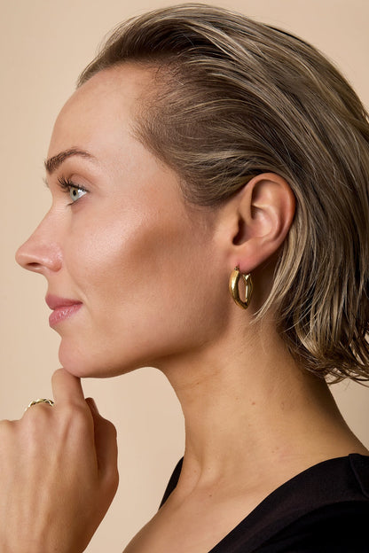 Woman wearing gold textured chunky hoop earrings and matching textured ring, showcasing youthful and aesthetic look