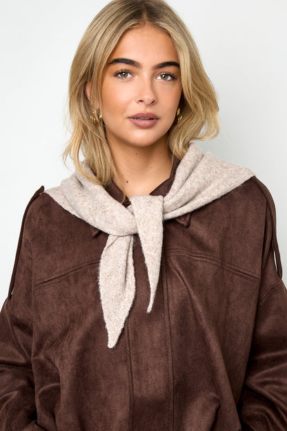 Woman wearing light beige knit scarf tied around neck over brown jacket