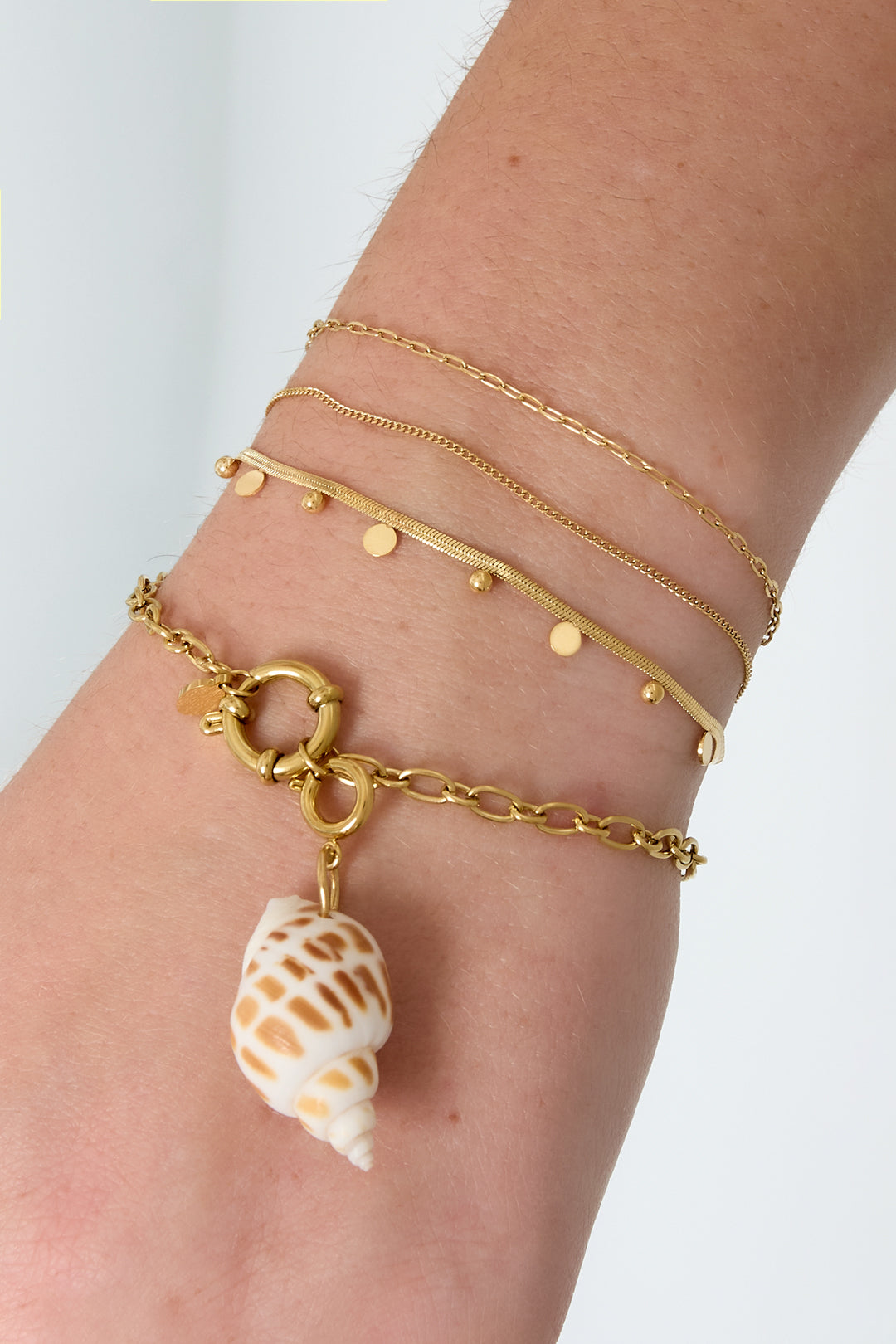 Gold layered chain bracelets with dot details and seashell charm worn on a wrist