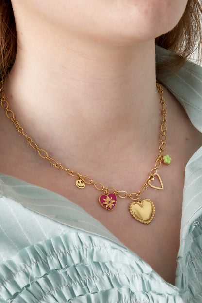 Close-up of gold-tone heart charm necklace worn on woman with light blue shirt, showing colorful charms and delicate chain