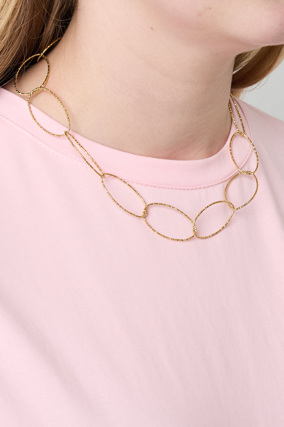 Side view of woman wearing gold chunky oval link necklace over light pink shirt