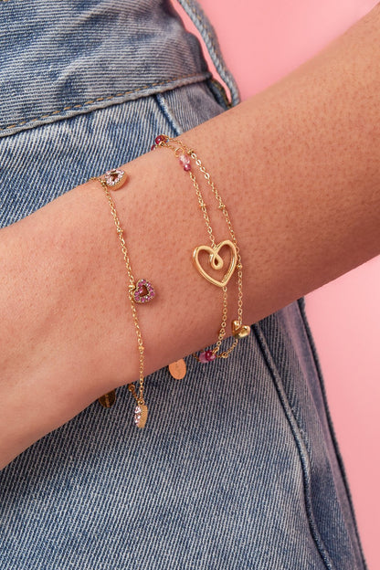 Gold chain bracelet on a wrist, featuring a hammered heart link and small pink pavé heart charms.