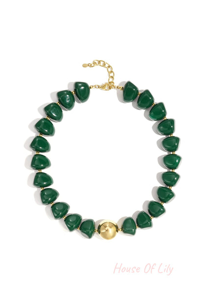 Close-up of a chunky green beaded necklace with gold clasp and centerpiece bead on white background