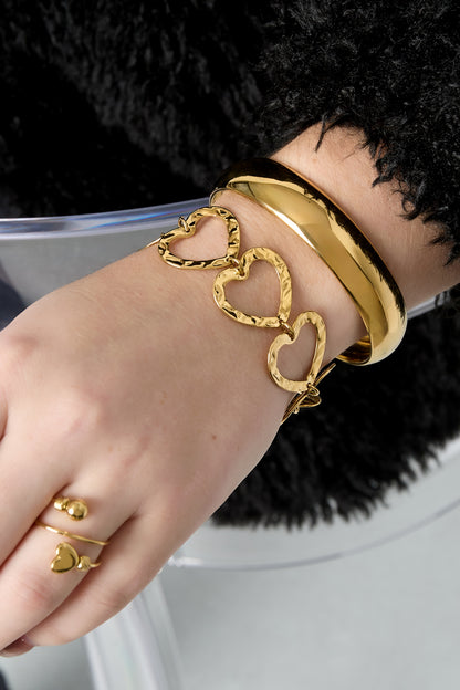 Woman's wrist wearing stacked bracelets including the hammered heart link bracelet in gold-tone metal and a smooth gold bangle