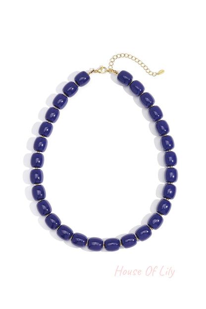 Close-up of navy chunky acrylic bead necklace with gold-tone chain extension on white background
