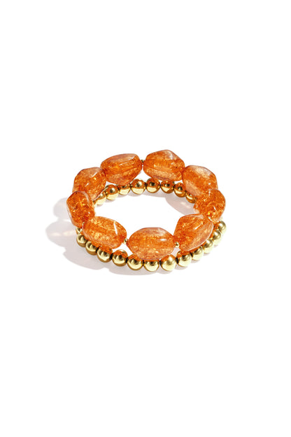 Close-up of orange chunky beaded bracelet set with glossy acrylic and gold-tone beads on white background