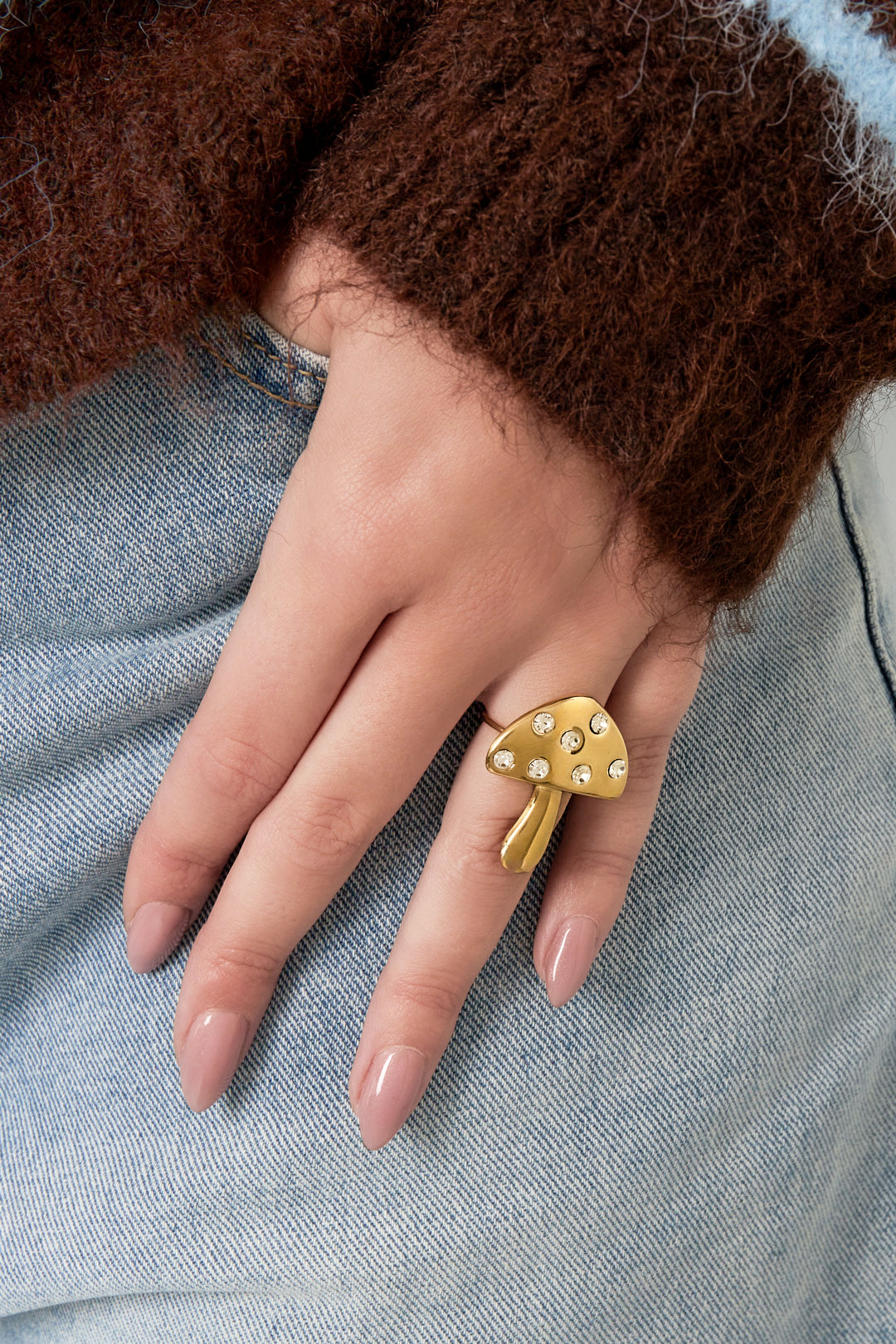 Woman wearing gold mushroom-shaped rhinestone ring styled with casual denim and brown fuzzy sweater