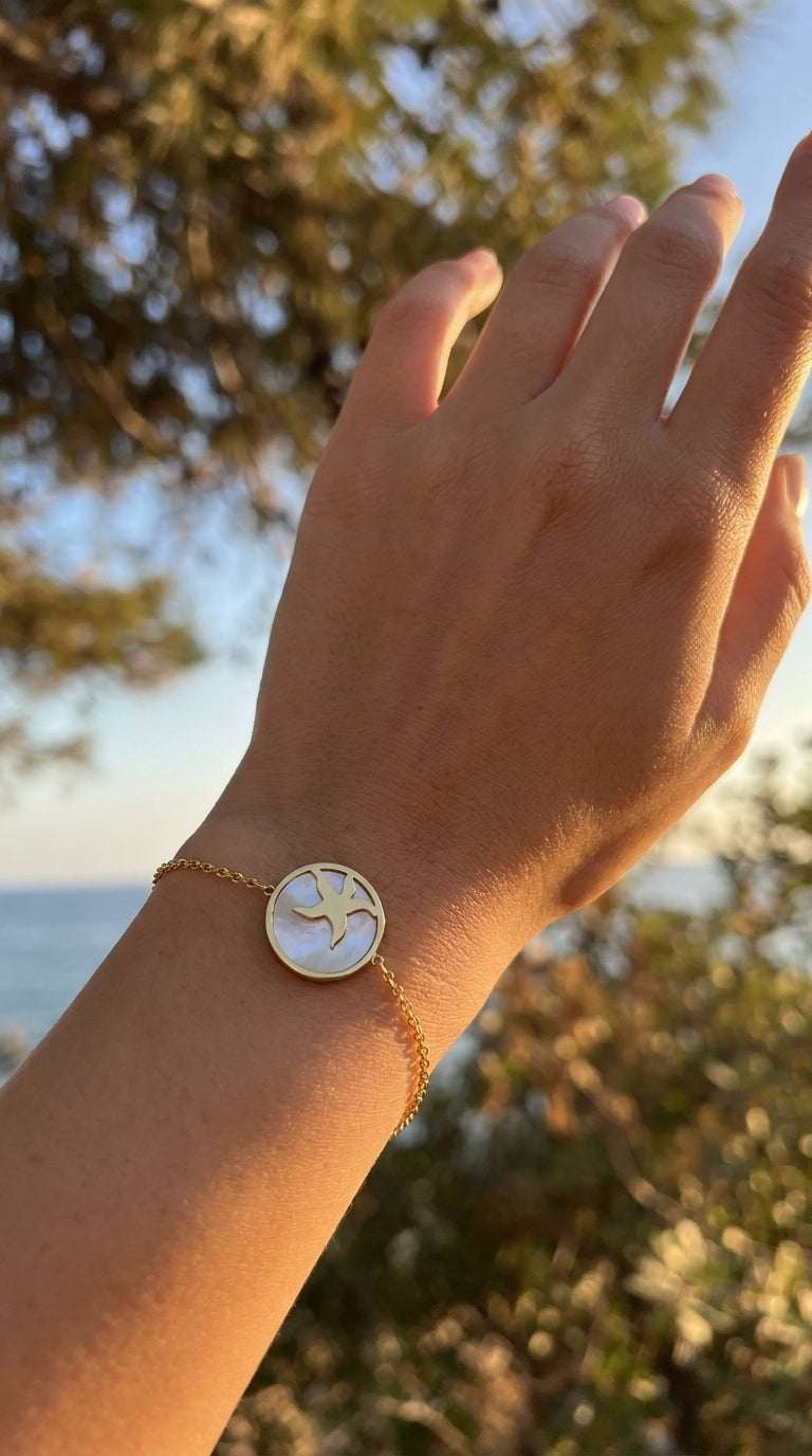 Gold chain bracelet featuring a round pendant with a mother-of-pearl inlay and a gold cutout starfish design.