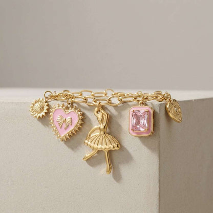 Gold chain bracelet with charms: sunflower, pink heart with bow, ballerina, pink emerald-cut stone, and evil eye.