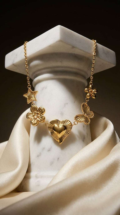 Gold chain necklace with charms of a star, flowers, heart, and butterfly draped over a white marble column.