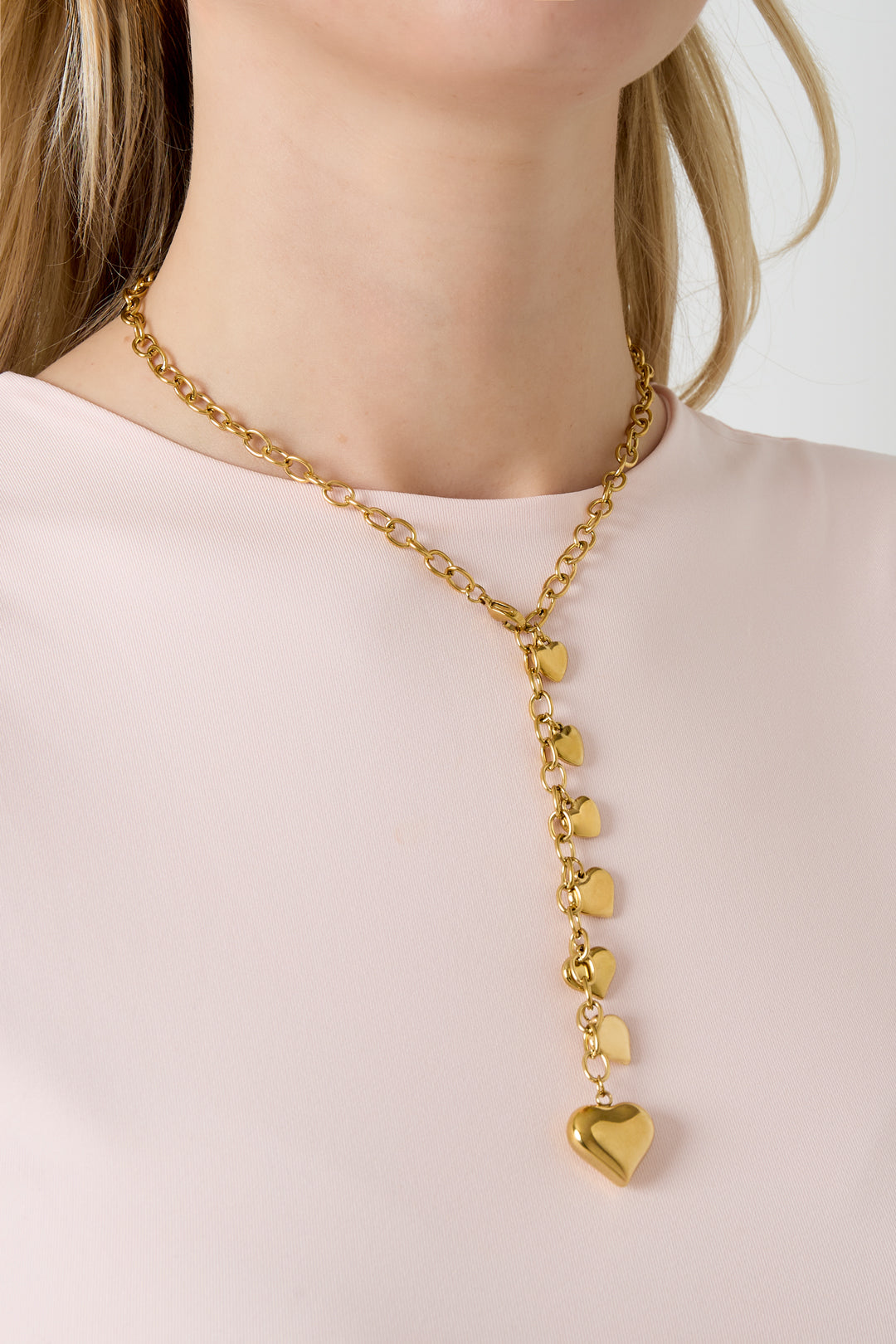 Model wearing a gold-tone heart charm necklace with cascading hearts, styled with a light pink top