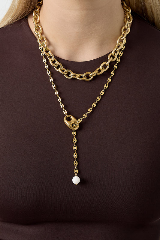 Model wearing layered necklaces with a chunky gold chain necklace and a longer gold pendant chain over a dark top