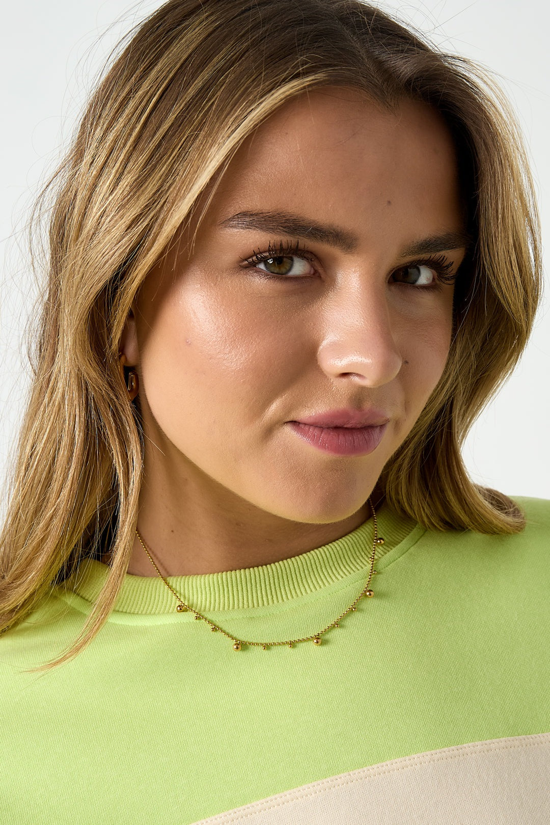 Young woman wearing the gold tone polka dot necklace styled with a lime green sweater, smiling softly
