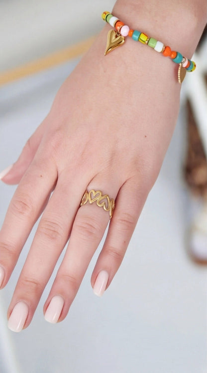 Hand wearing a gold ring and colorful beaded bracelet on a light background
