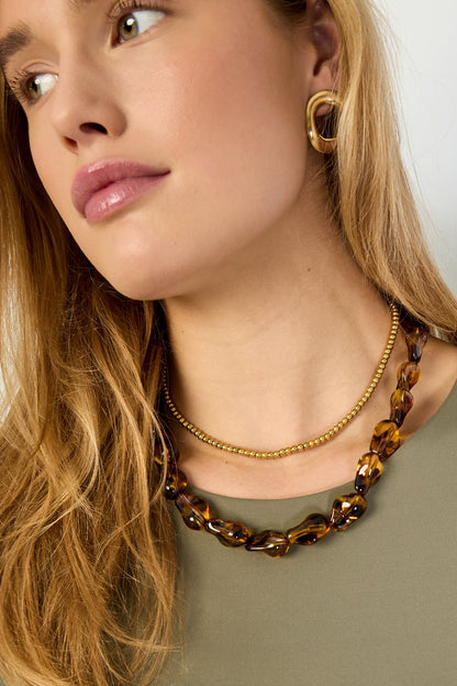 Close-up side profile of woman wearing tortoiseshell acrylic necklace with gold earrings and olive green top