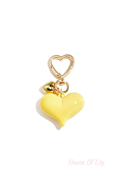 Single yellow acrylic heart bag charm with gold heart clasp and mini gold heart pendant on white background