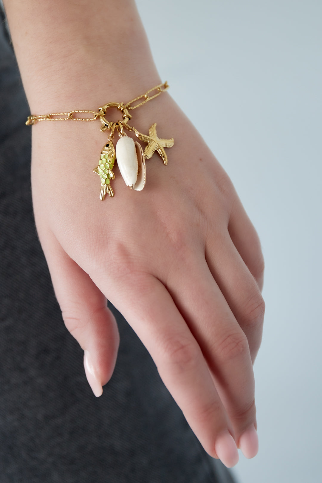 Close-up of a woman's wrist wearing the gold-plated charm bracelet with dangling ocean-inspired charms