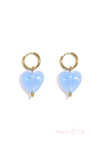 Pair of gold hoop earrings with light purple glossy resin heart pendants on white background