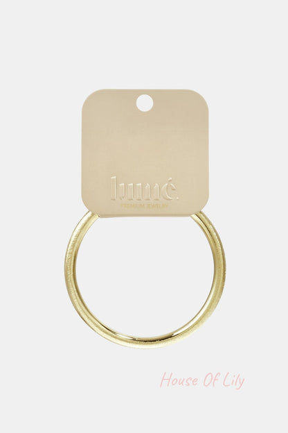 Gold-toned brushed metal circle bangle on a branded beige jewelry display card.