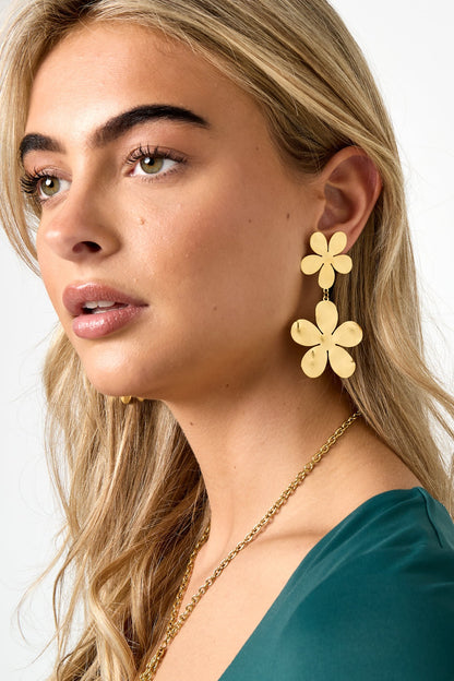 Close-up side view of woman wearing bold gold floral drop earrings paired with a green top and gold chain necklace