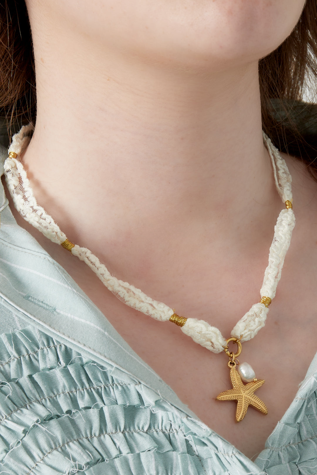 Close-up of woman wearing cream lace necklace with gold starfish and pearl charm over blue ruffled top